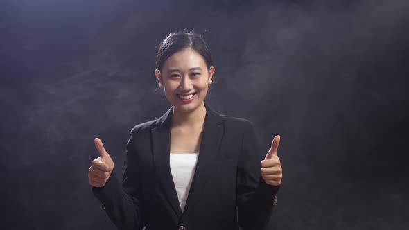 Smiling Asian Speaker Woman Showing Thumbs Up Gesture To Camera While Standing In The Black Studio alt