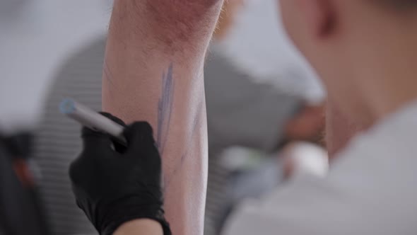 Young Man Drawing a Sketch for Tattoo on the Leg on His Client in the Salon alt
