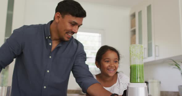 Hispanic father with smiling daughter teaching making smoothie in blender alt