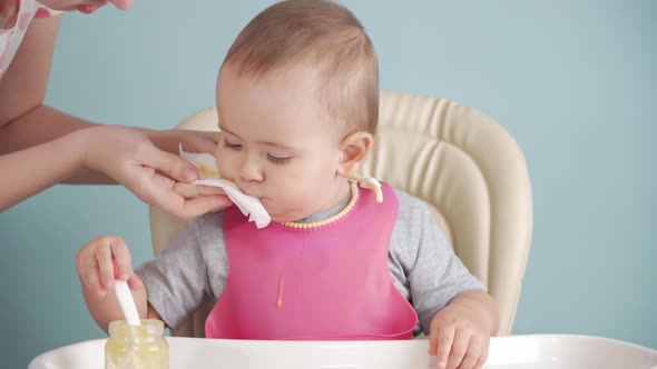Mom wipes the baby's face with a napkin sitting on a feeding chair alt