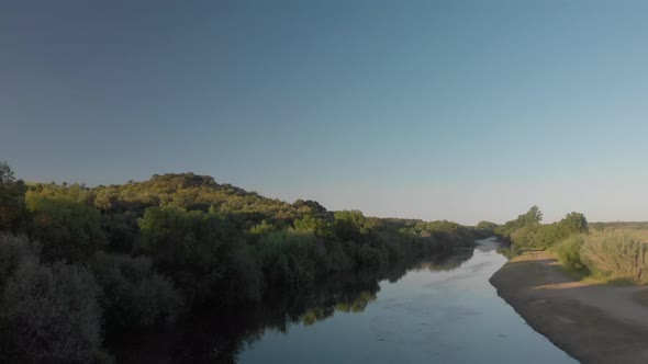 Drone shot of a calm river surrounded by trees during sunset alt