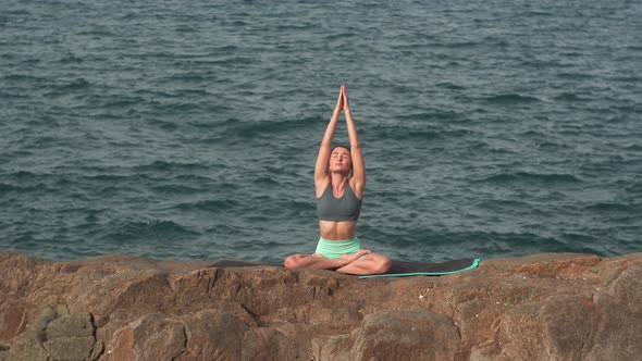 Young Woman Tries Yoga in Lotus Position on Rock Against Sea