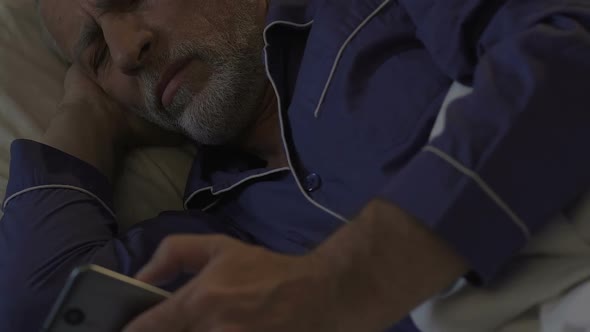 Aged Man Lying in Bed Awake at Night Scrolling Mobile Phone, Problems with Sleep alt