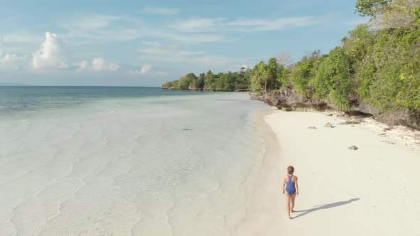 Aerial: woman walking on tropical island turquoise water white sand beach alt