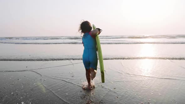 Little Girl Is Running on the Sea To Waves Holding Surfboard in Her Hands