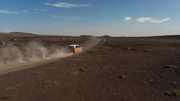 Car Moving on Dirt Road Leading Through Barren Volcanic Plain alt