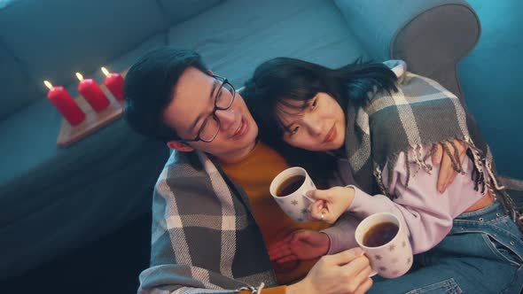Happy Young Couple Drinking Tea Covered with Blanket with Lights of Candles alt