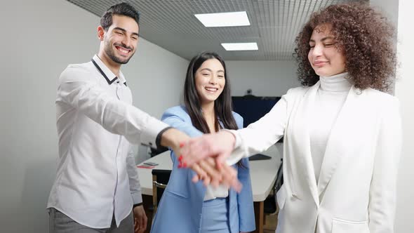 Positive Laughing Young Millennial Multiracial Coworkers Stacking Hands in Office alt