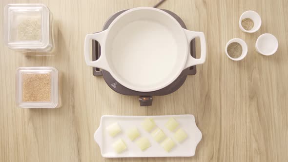 Female chef pouring milk in a cooking pot on an electric stove, top shot static alt