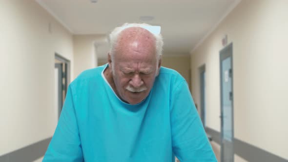 Old patient with walking frame going through hospital corridor