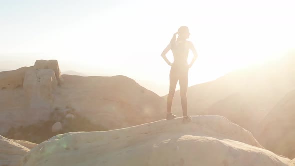 Woman hiker stands on mountain top in sunlight alt