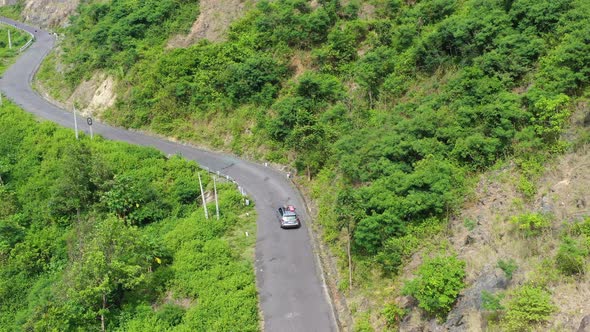 Aerial drone footage tracking an SUV car flying over an empty curve road