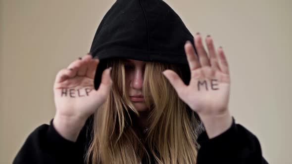 Teenage Girl Covering Her Face with a Hood Shows Her Palms with the Inscription HELP ME alt