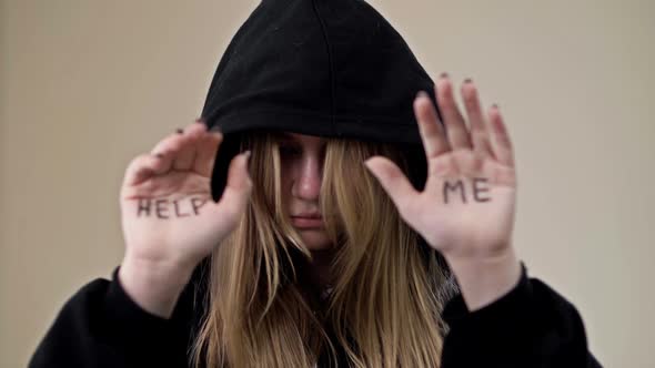 Teenage Girl Covering Her Face with a Hood Shows Her Palms with the Inscription HELP ME