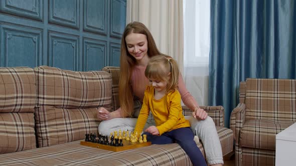 Small Cute Daughter Child and Young Mother Playing Chess at Home Sofa Leisure Hobbies Activities alt