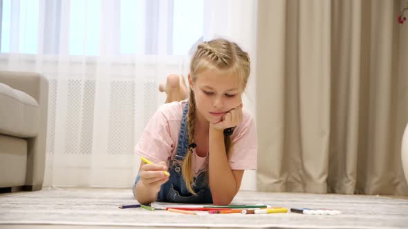 Cute Preteen Girl Lying on Floor and Drawing on Paper in Living Room
