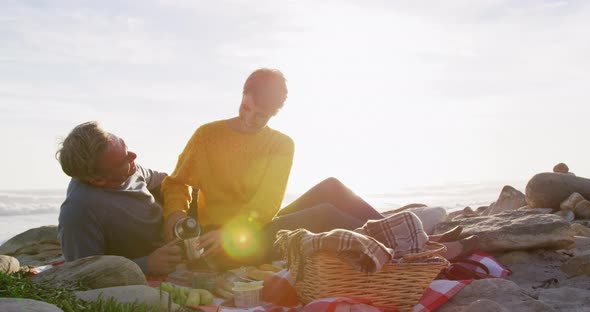 Caucasian couple enjoying free time by sea on sunny day eating and drinking coffee alt