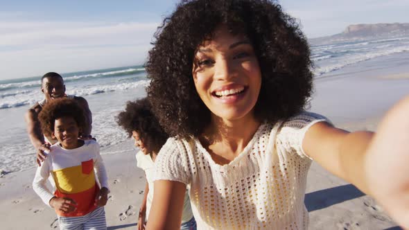 Smiling african american parents and their children taking a selfie with smartphone on the beach alt