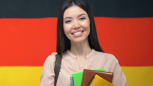Smiling Female With Notebooks on German Flag Background, Academy Course, Student alt