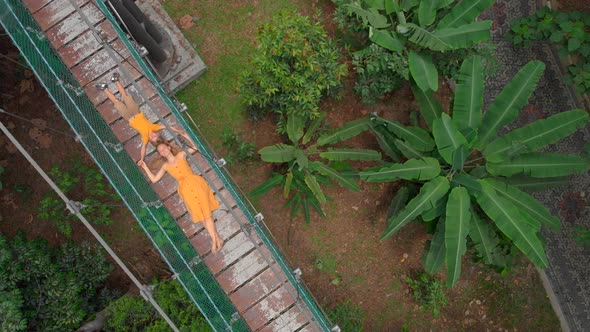 Aerial Shot of a Young Woman and Her Little Son Laying on a Suspension Bridge Over the Jungles alt