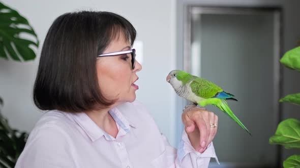 Mature Woman at Home with a Pet Parrot on Her Arm alt