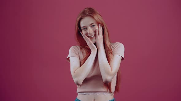 Excited Redhaired Young Woman of 20 Years in a Pink Casual Tshirt Isolated on a Pink Background alt