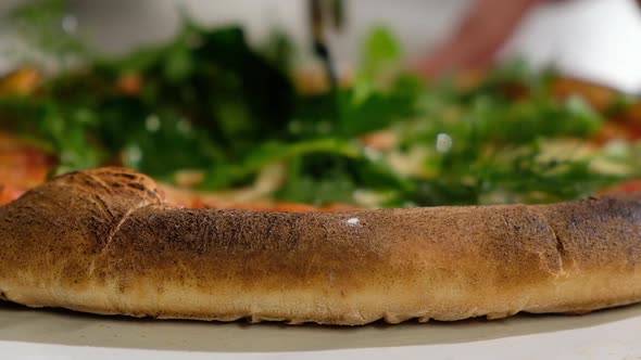 baker cuts fresh hot pizza with aromatic herbs with a round knife before serving
