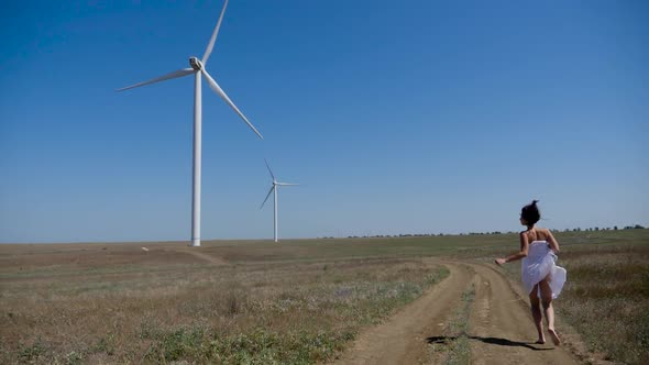 Girl in a White Coat Runs Through a Field with Windmills alt