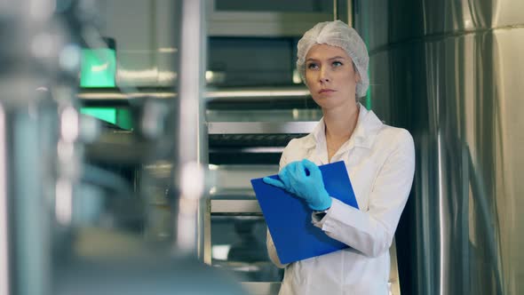 Female Factory Worker Is Filling in a Chart Board Working at Modern Factory Facility. alt