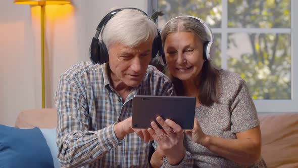 Happy Elderly Man and Woman in Headphones Watching Video on Tablet Pc at Home alt