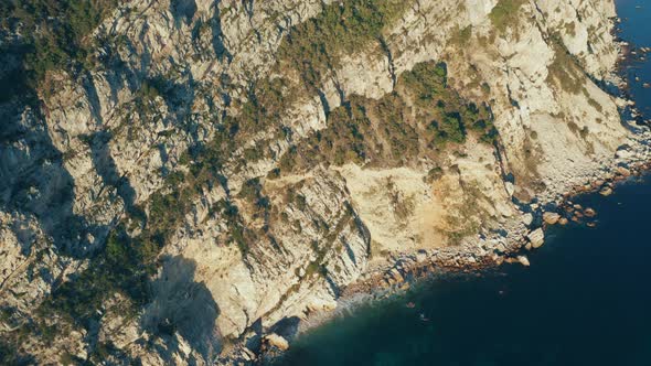 Panoramic view of steep stone coastal cliffs with evergreen trees and bushes on the slopes