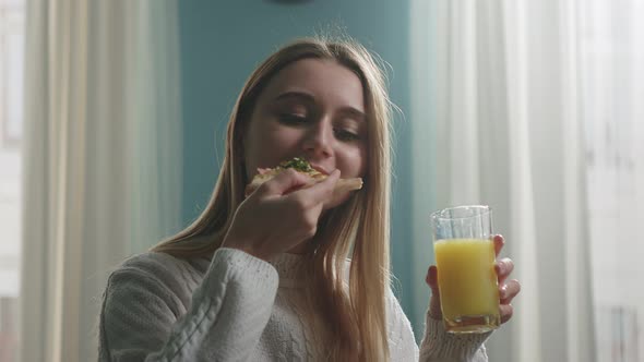 Young girl in white sweater eats pizza and drinks orange juice