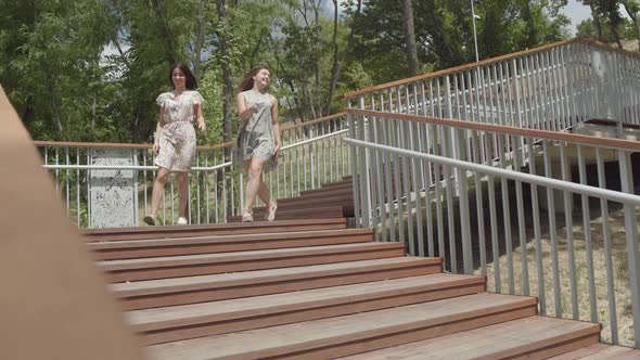 Two Attractive Girls Wearing Summer Dresses Running Down the Stairs in the City Park alt