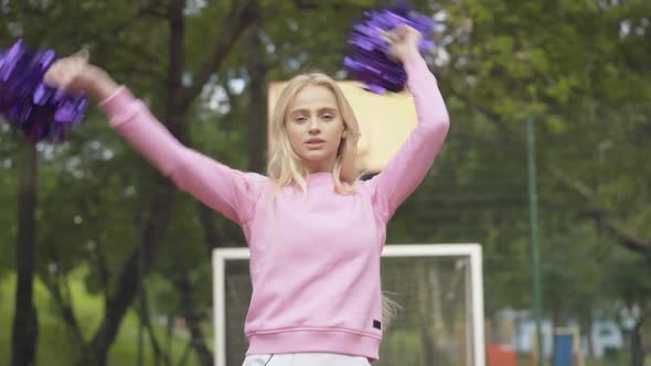 Blond Confident Woman Dancing with Pom-poms on Outdoor Court. Portrait of Positive Confident alt