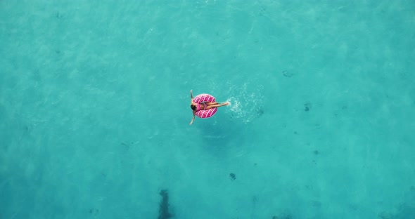 Aerial view of a young woman swimming with the donut swim ring in clear blue sea