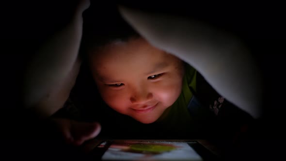 Night shot of Happy little asian boy playing with tablet or smartphone