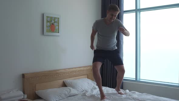 Handsome Man Have Fun Jumping Dancing on Bed By the Window
