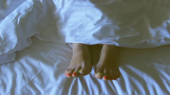 Female Feet on the White Bed Under Blanket