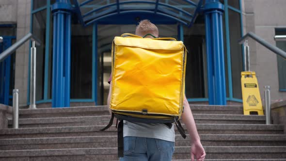 Back View Male Young Courier Walking Upstairs Entering Business Center in Urban City Outdoors alt