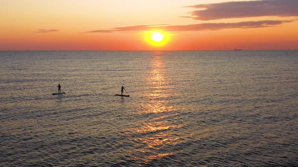 Young woman silhouette on a stand up paddle board. Sunset light in the water. alt