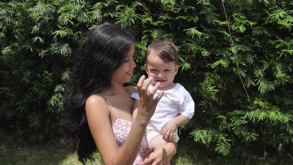 A Darkhaired Woman Stands in a Green Garden with a Small Child in Her Arms