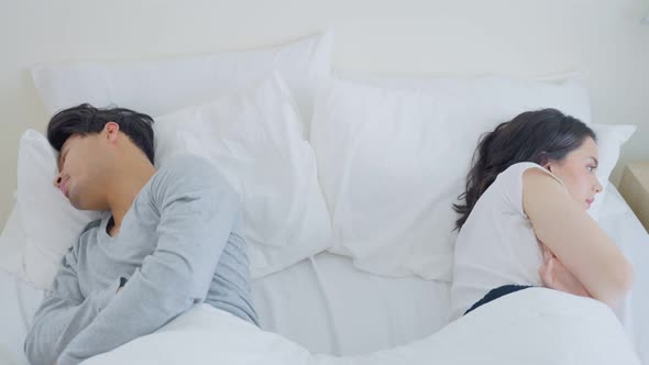 Asian young couple lying down on bed feel heartbroken with painful after fight argument in bedroom. alt