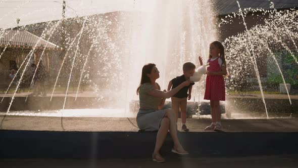 Boy Bites Cotton Candy with Mother and Sister Near Fountain alt