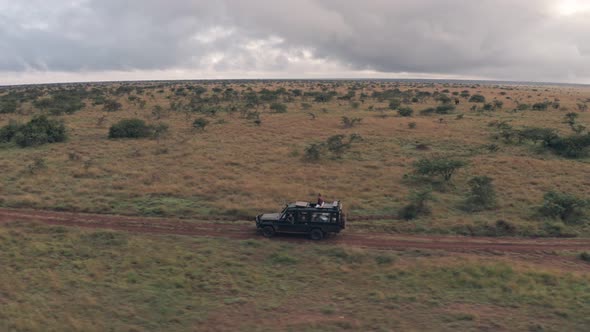 Woman sitting on top of 4 wheel drive while on wildlife safari holiday in Kenya. Aerial drone view alt