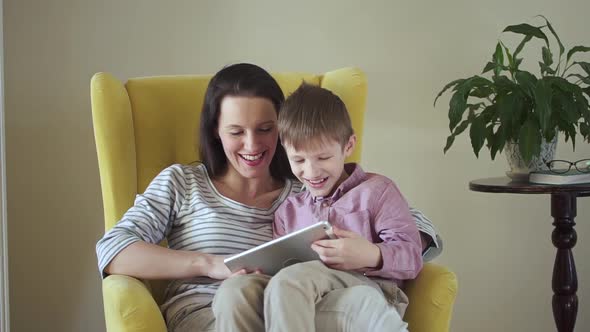 Caucasian Woman and Child Using Digital Gadget While Sitting on Chair in Apartment Room Spbd alt