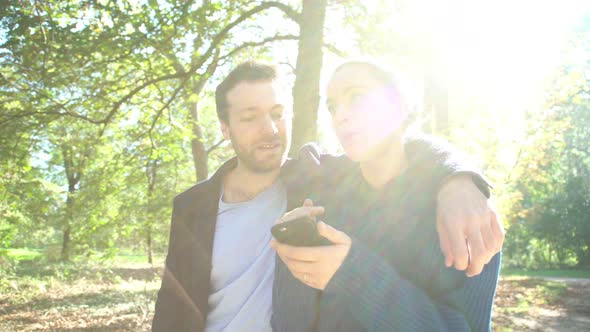 Couple looking at smartphone while strolling through park alt