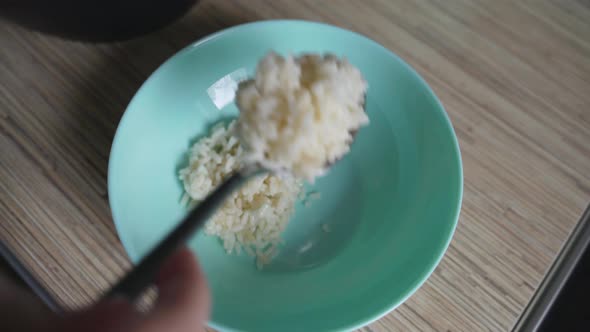 Woman Puts Fresh Steamed White Rice Into Deep Blue Plate with Spoon alt