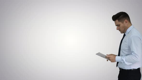 Elegant Young Businessman Using Tablet While Walking on Gradient Background. alt