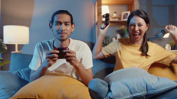 Happy asia young couple man and woman sit couch use joystick controller play video game.