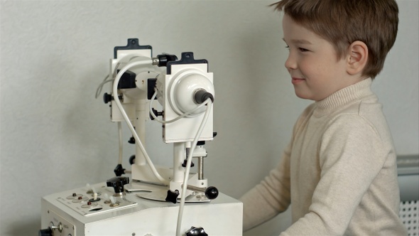 Old male doctor examines eyes of boy through slit lamp